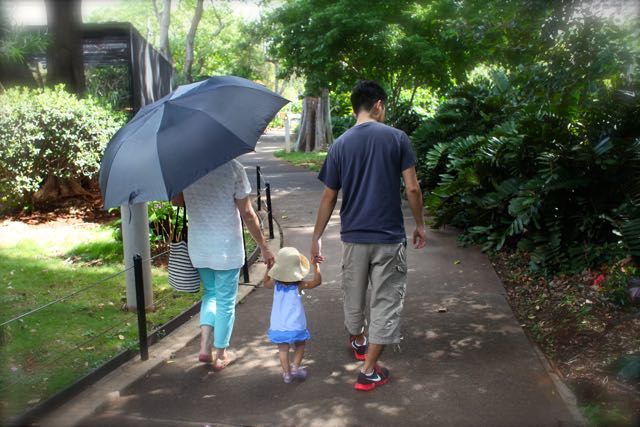 two parents with a little girl in beteween walk hand in hand down a garden path